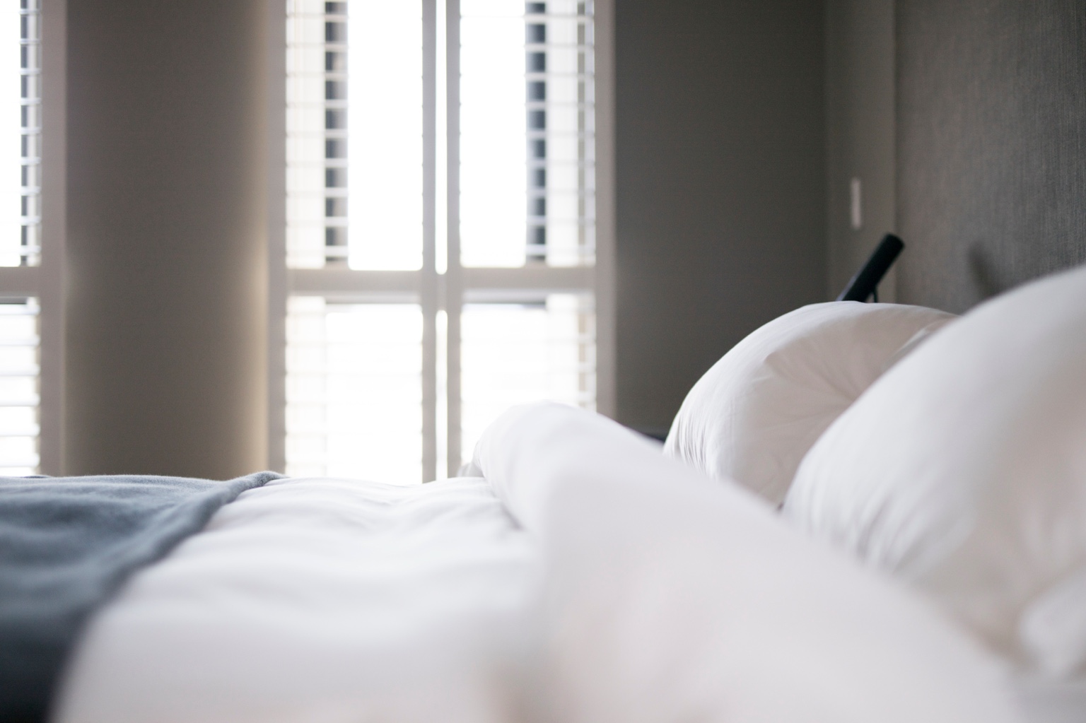 Cama branca preparada para hóspedes em alojamento local, com roupa de cama limpa e ambiente luminoso.