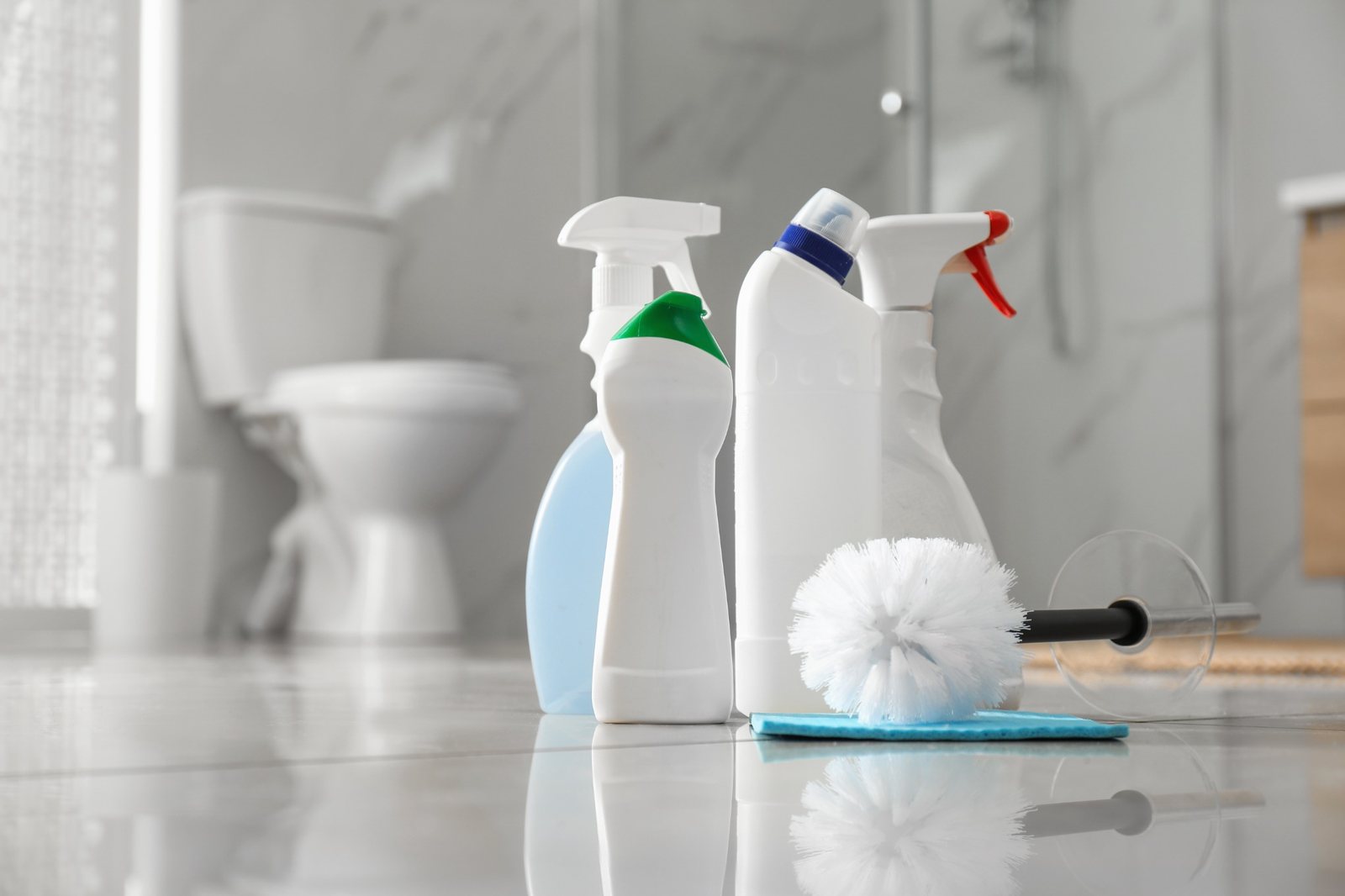 Produtos de limpeza alinhados sobre o chão de uma casa de banho, prontos para higienização rigorosa